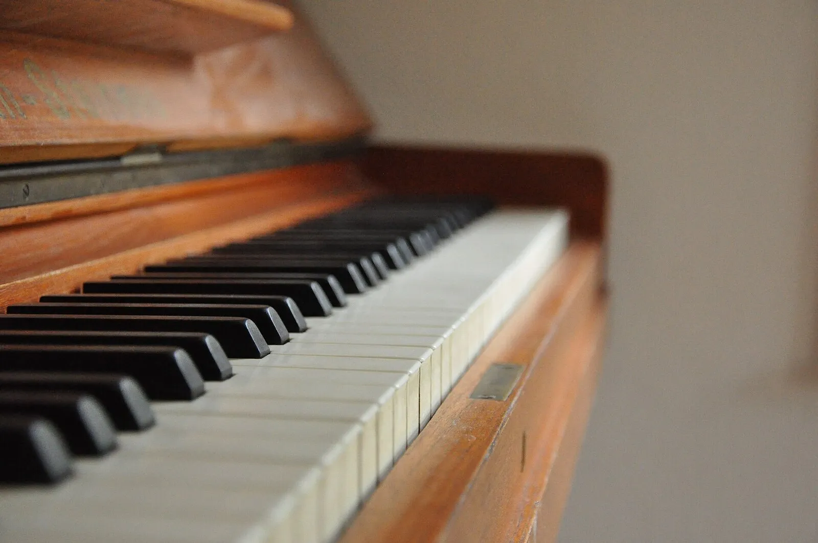 Tastiera di un pianoforte verticale in legno chiaro vista di scorcio, con i tasti neri in primo piano