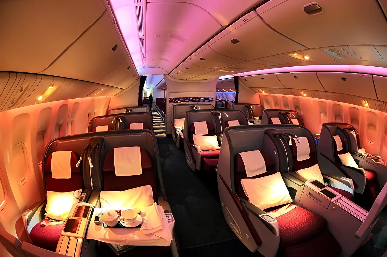 Cabina business di un Boeing 777 di Qatar Airways con file di poltrone reclinabili e cuscini bianchi