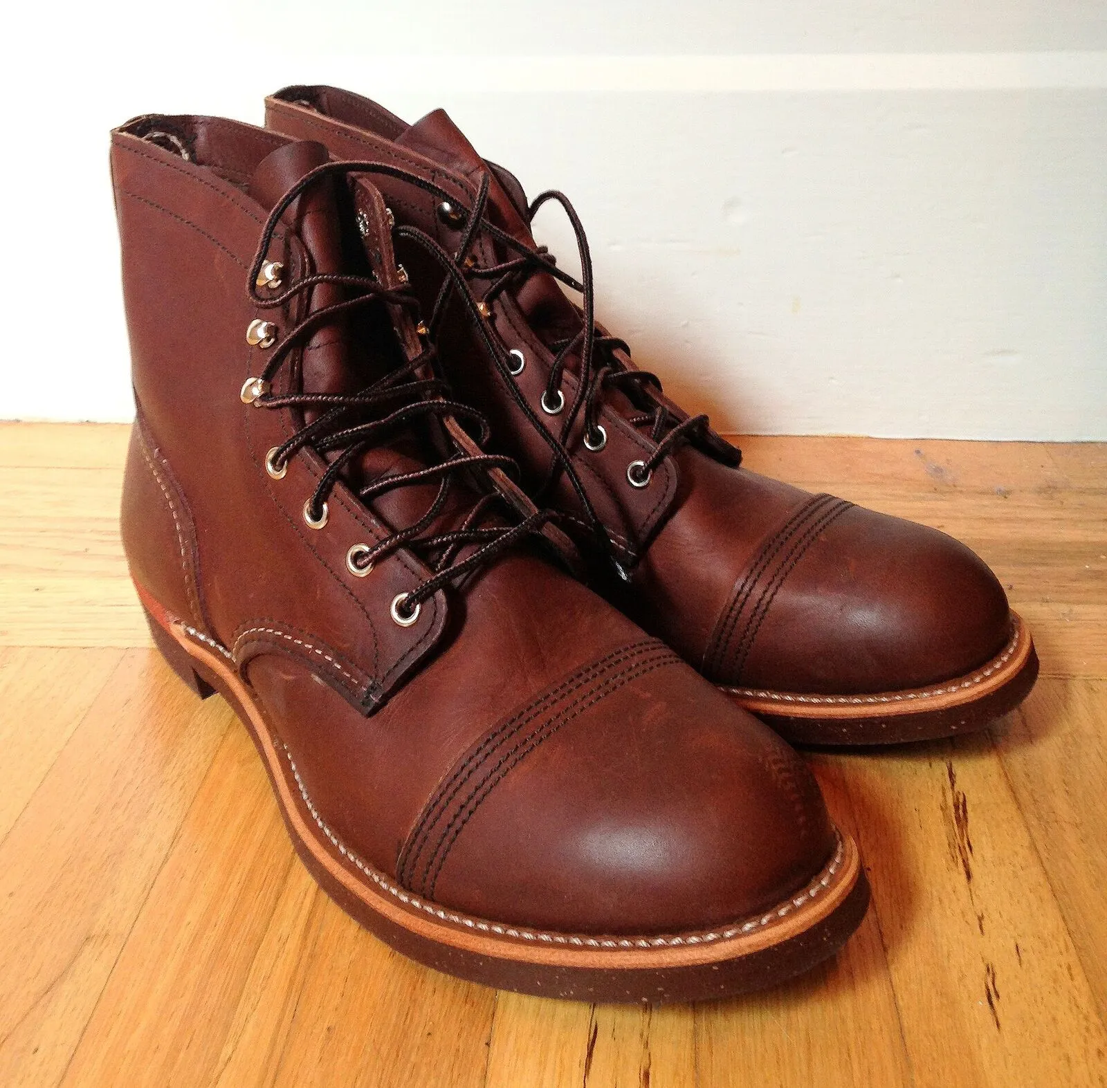 Un paio di stivali Red Wing Iron Ranger in pelle marrone appoggiati su un pavimento di legno